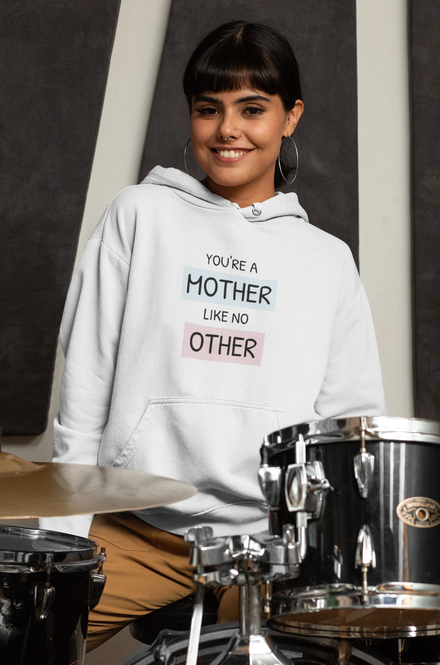 Person wearing a hoodie with text in front of a drum set