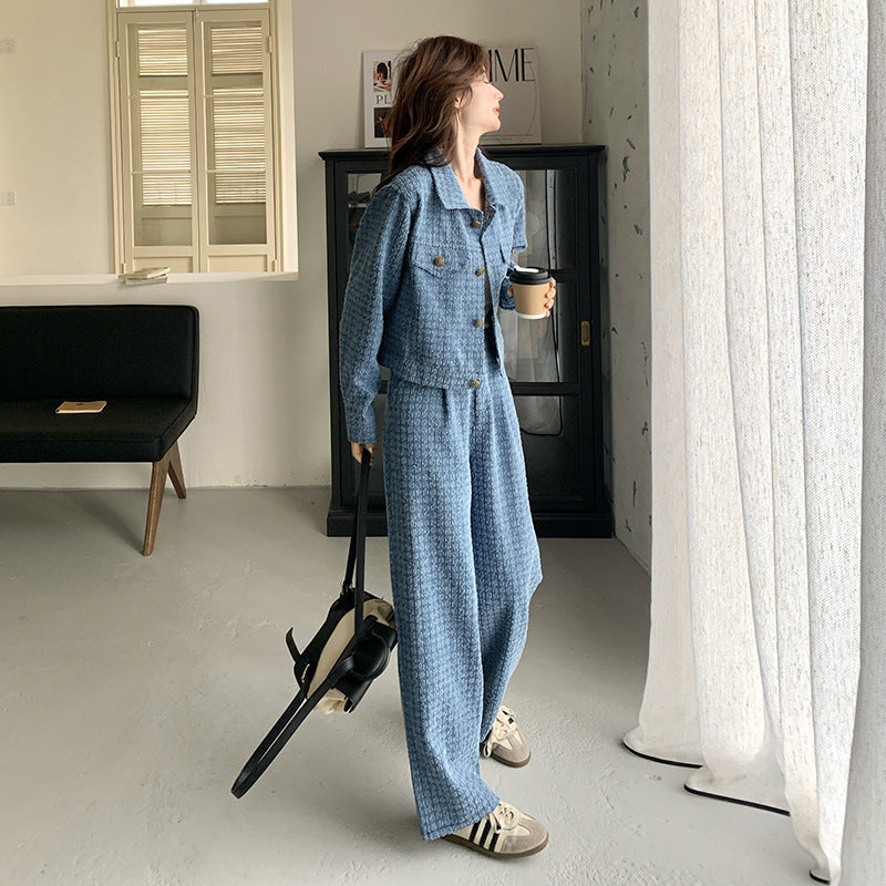 Person in a blue outfit holding a coffee cup and a dog leash in a room with a white wall and a window.